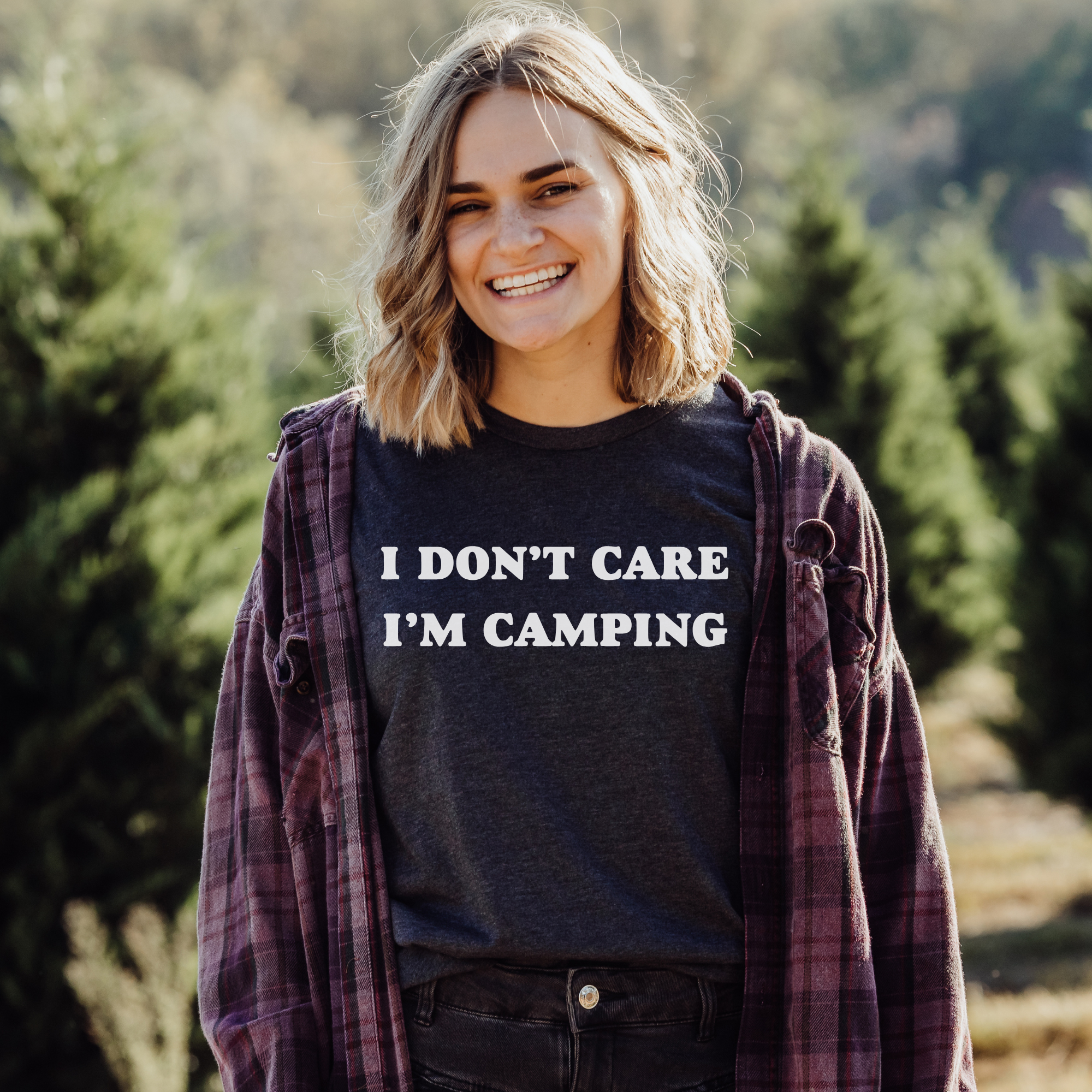 Person wearing a shirt with 'I Don't Care I'm Camping' text in a forest setting